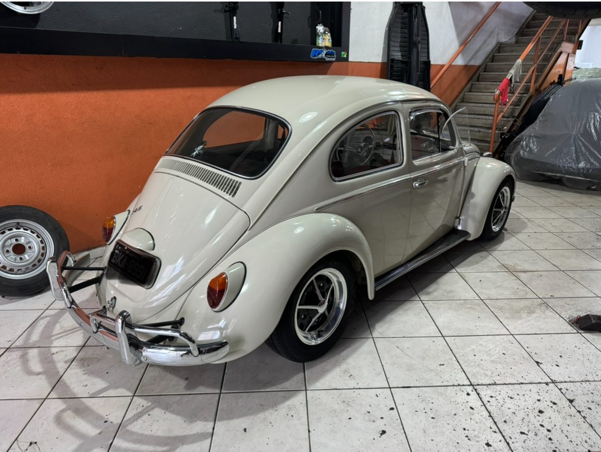 Fusca bege dentro da oficina, ao lado da parede laranja